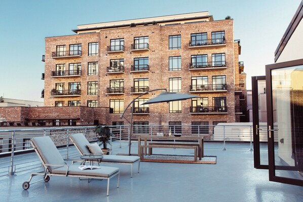 A rooftop terrace with lounge chairs, a table, and a large umbrella. - The Luzianne (New Orleans)