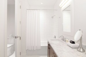 A modern bathroom with a bathtub, a shower, a toilet, and a vanity with a mirror. - The Luzianne (New Orleans)