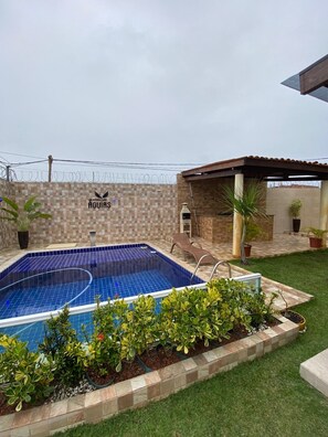 A swimming pool with a tiled deck, surrounded by potted plants and a small covered seating area. - Beach house: Swimming pool, gourmet area and pergola. (Camaçari)