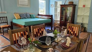 Un comedor con una mesa dispuesta para seis personas, rodeada de sillas de madera con cojines a rayas. Se aprecia un aparador con puertas de cristal en el fondo.