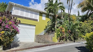 Edificio residencial con puerta de garaje, rodeado de exuberante follaje y plantas con flores.