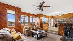 A spacious living area with a sofa, coffee table, and a fireplace. Large windows provide natural light and views of the outdoors. - Conrad Vista | Fully Remodeled Waterfront Retreat (Priest River)