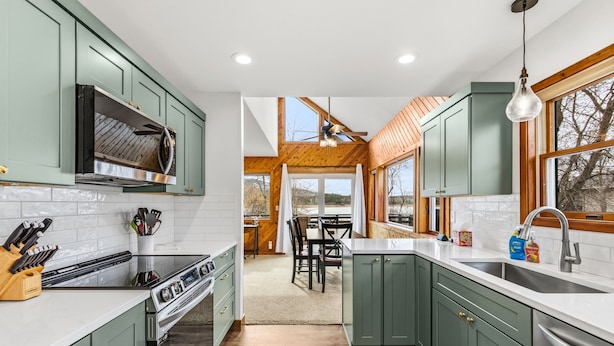 A modern kitchen with green cabinets, a stainless steel range, and a large window providing natural light. - Conrad Vista | Fully Remodeled Waterfront Retreat (Priest River)