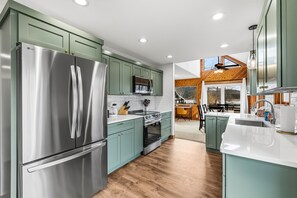 A modern kitchen with stainless steel appliances, teal cabinetry, and a wooden dining area.