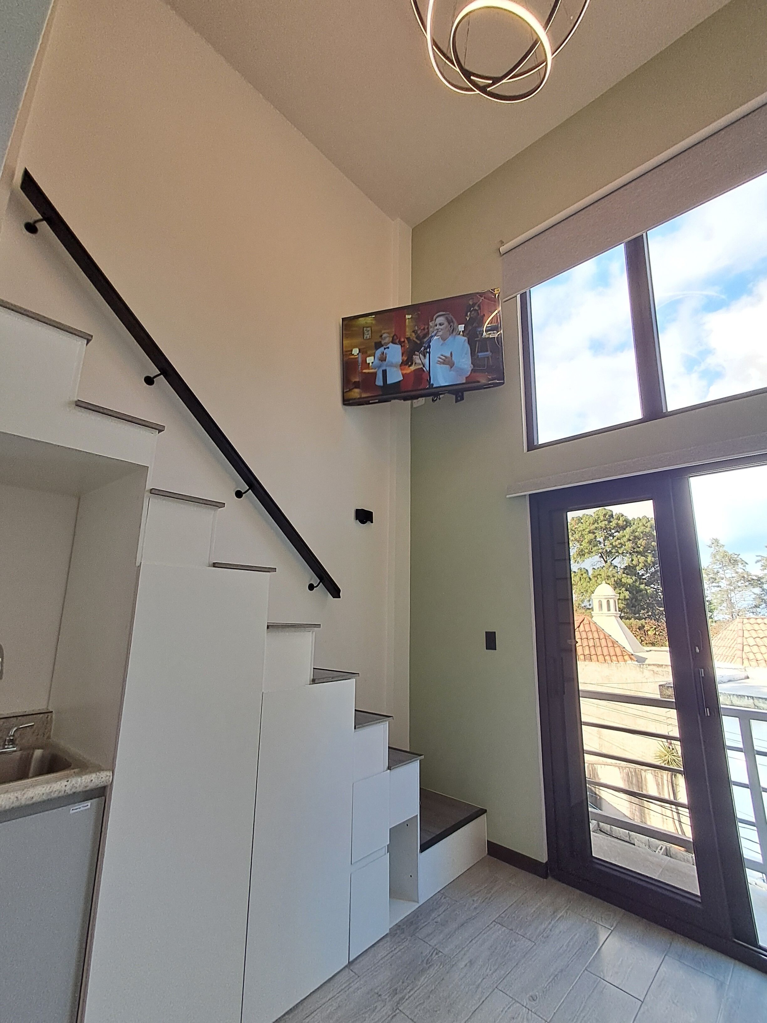 Una escalera moderna con barandilla negra, techo plano y un ventanal grande con vistas al exterior.