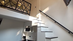 Una cocina moderna con una escalera que lleva a un balcón, una lámpara colgante y un televisor instalado en la pared.