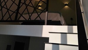 Un intérieur moderne avec une cloison aux motifs géométriques, un escalier et un lit situés à l’étage supérieur.