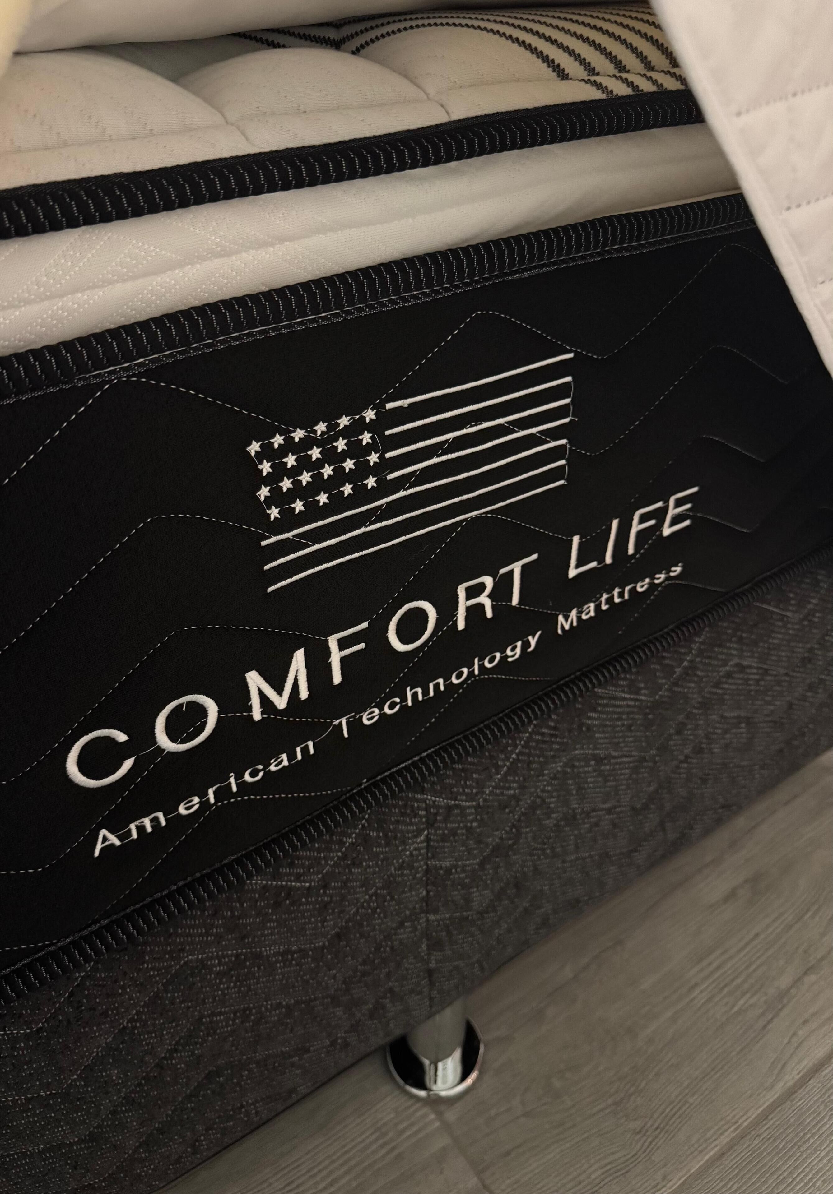 A mattress with the text "COMFORT LIFE American Technology Mattress" and an American flag design.