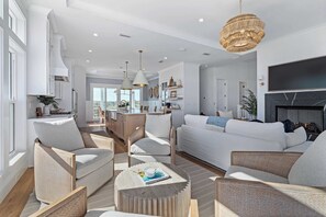 Ein geräumiges Wohnzimmer mit einer großen Couch, Sesseln und einem Couchtisch. Ein Kamin und ein an der Wand befestigtes Fernsehgerät sind ebenfalls vorhanden.