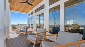 A covered outdoor deck with wooden furniture and large windows offering views of the surrounding area. - Seaclusion l Luxury l Heated Pool l Beach (St. Augustine)
