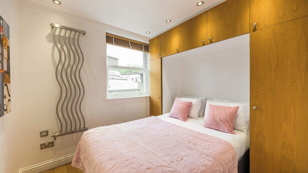 A bedroom with a bed, a window, and a wooden wardrobe. - A Midtown Minute - Holborn - by Frankie Says (London)
