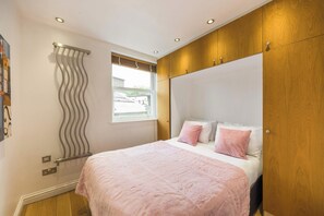 A bedroom with a bed, a window, and a wooden wardrobe. - A Midtown Minute - Holborn - by Frankie Says (London)