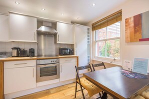 A modern kitchen with white cabinets, stainless steel appliances, and a wooden dining table. - A Midtown Minute - Holborn - by Frankie Says (London)