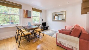 A room with a dining table, chairs, a sofa, a TV, and a large window. - A Midtown Minute - Holborn - by Frankie Says (London)