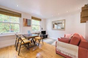 A room with a dining table, chairs, a sofa, a TV, and a large window. - A Midtown Minute - Holborn - by Frankie Says (London)