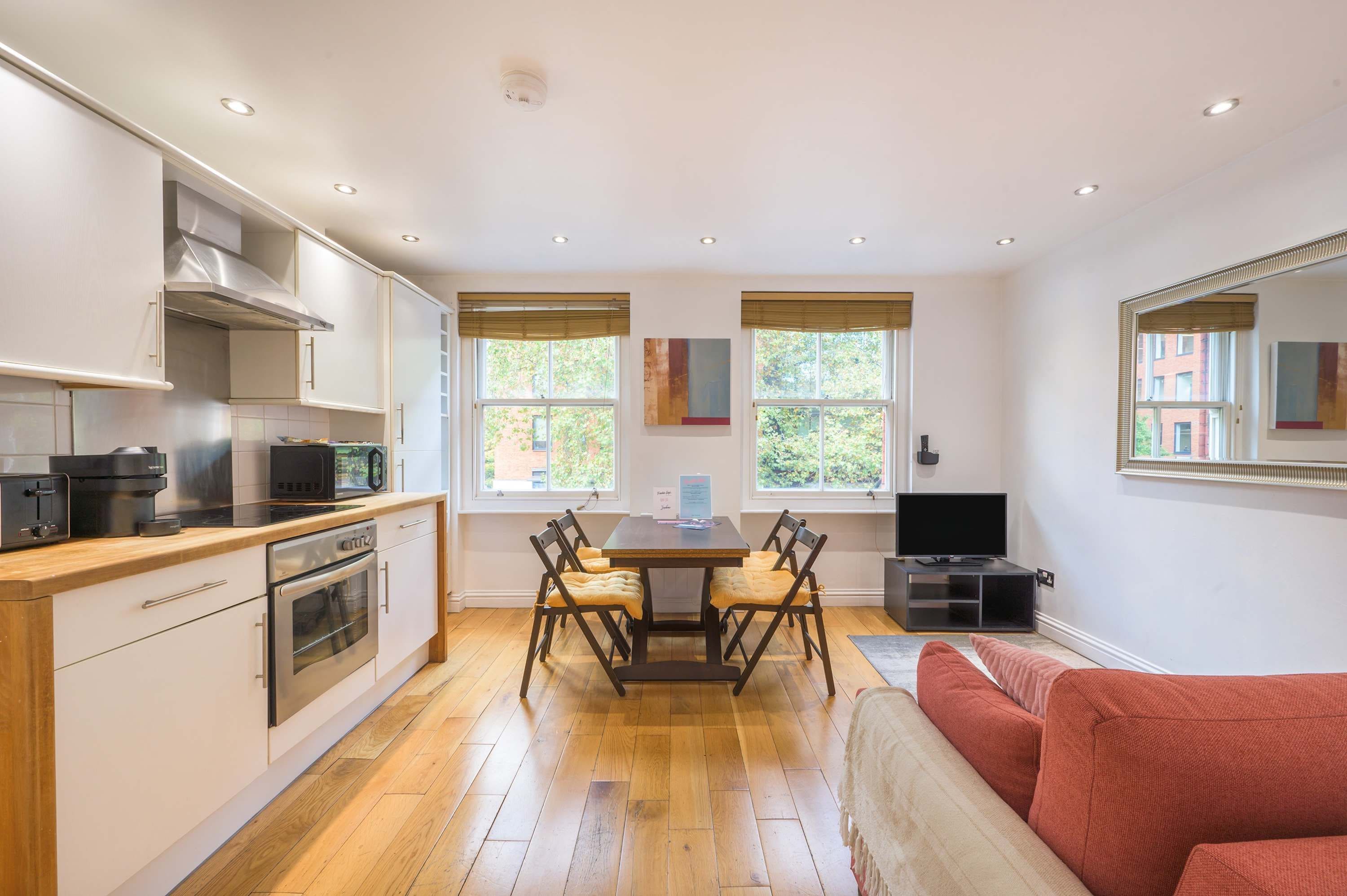 A modern kitchen with built-in appliances, a dining table with chairs, and a large mirror.