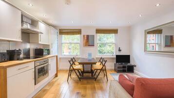 A modern kitchen with built-in appliances, a dining table with chairs, and a large mirror.
