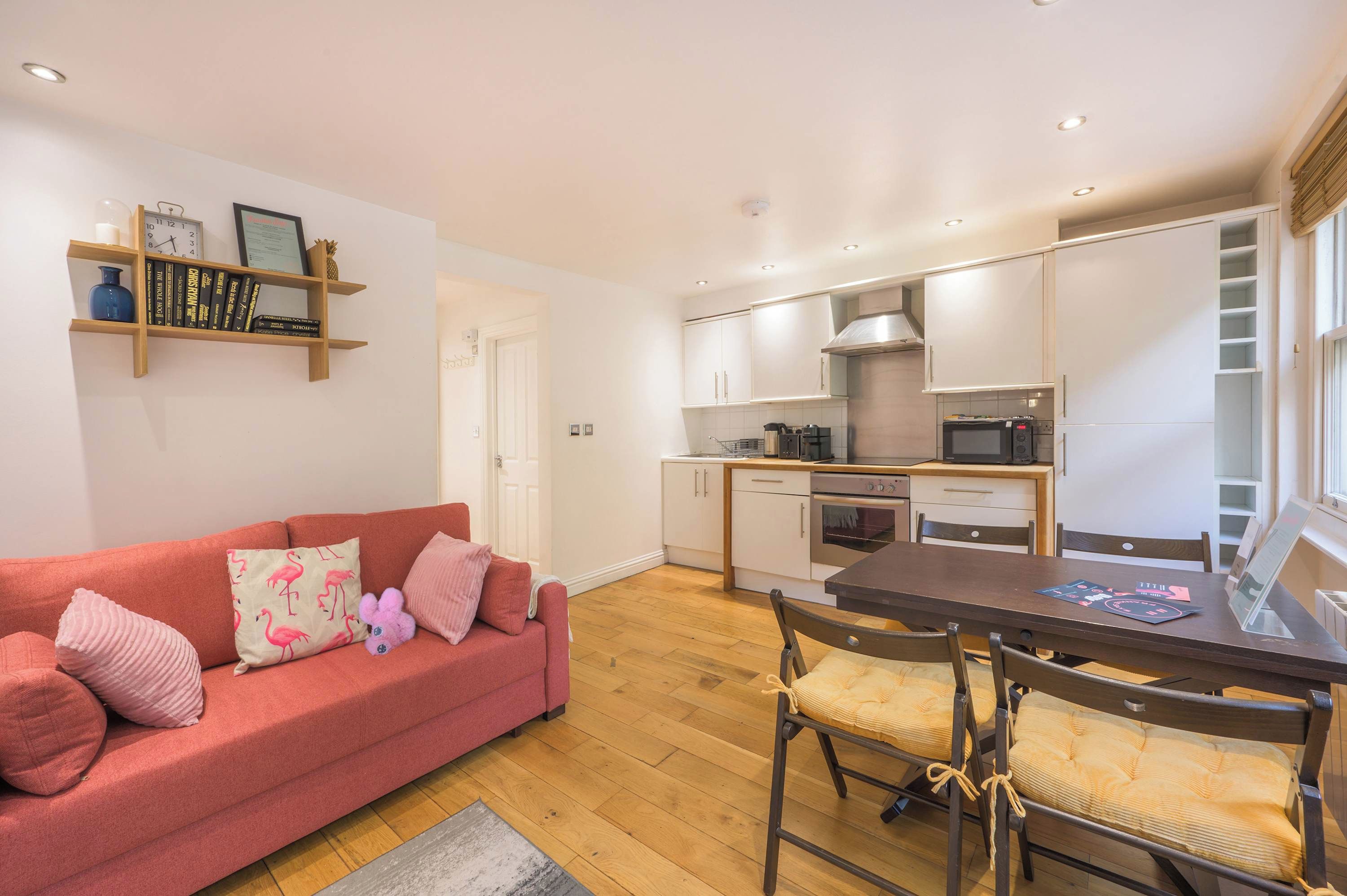 A compact living space with a kitchenette, a sofa with pink cushions, and a dining table with chairs.