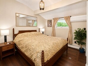 Een slaapkamer met een groot bed, een nachtkastje, een spiegel, een raam met gordijnen en een kamerplant.