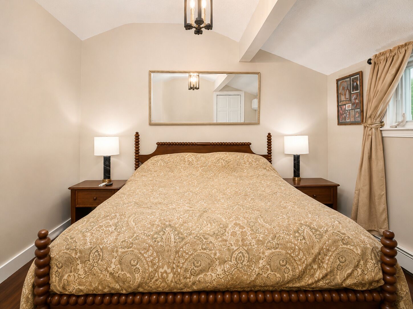 Une chambre à coucher comprenant un lit, deux tables de chevet, une commode, un miroir, une fenêtre avec des rideaux et un lustre.