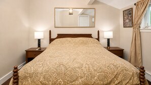 Une chambre à coucher comprenant un lit, deux tables de chevet, une commode, un miroir, une fenêtre avec des rideaux et un lustre.