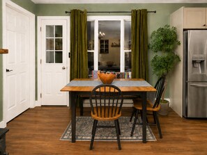 A dining area with a wooden table, two chairs, a rug, a plant, and a refrigerator.