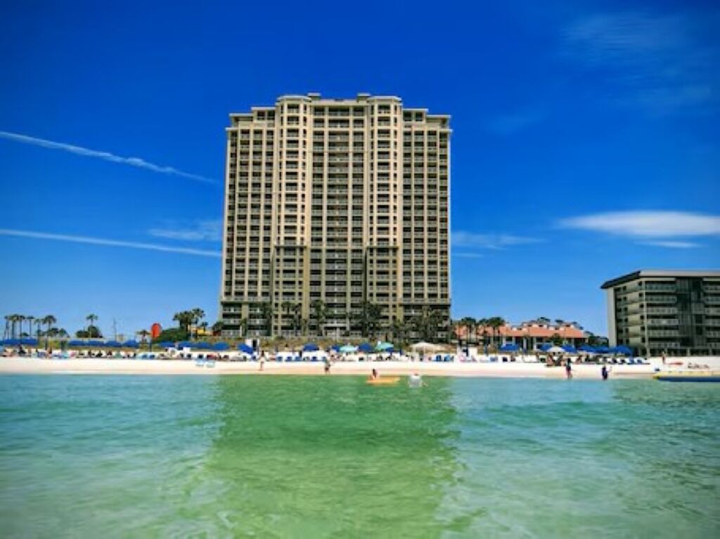 A tall hotel with a beach view, multiple balconies, and a pool area.