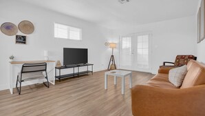Un salon moderne avec un plancher en bois, un canapé blanc, un téléviseur posé sur un meuble, un bureau avec une chaise et une lampe.