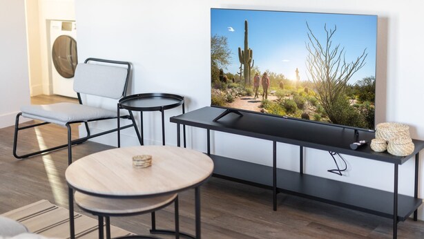 Un salon moderne avec un téléviseur à écran plat, un canapé gris, une table ronde en bois et un meuble TV noir.