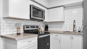 Une cuisine moderne avec des meubles blancs, une cuisinière en acier inoxydable, un four à micro-ondes et un évier.