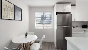 A modern kitchen with white cabinets, a stainless steel refrigerator, and a dining area with a white table and chairs. - King Bed near Midtown | Encanto Park (Phoenix)