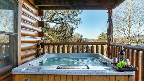 Ein Whirlpool mit Holzterrasse, Holzgeländer und Blick auf Bäume und Berge.