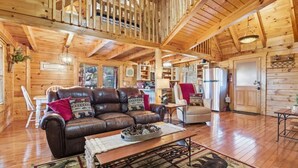 Ein Holzblockhaus-Interieur mit Ledersofa, Esstisch und Küchenzeile.
