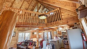 Ein Holzblockhaus-Interieur mit Schlafzimmer auf dem Schlafboden, einem Essbereich und einer Küche.