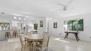 A spacious kitchen with white cabinets, a dining area with a round table and chairs, and a large window with a view of greenery. - Gull Cove (New Smyrna Beach)