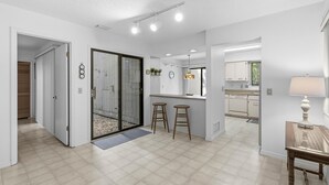A modern kitchen with white cabinets, a countertop, and a window. There are two stools and a table. - Gull Cove (New Smyrna Beach)