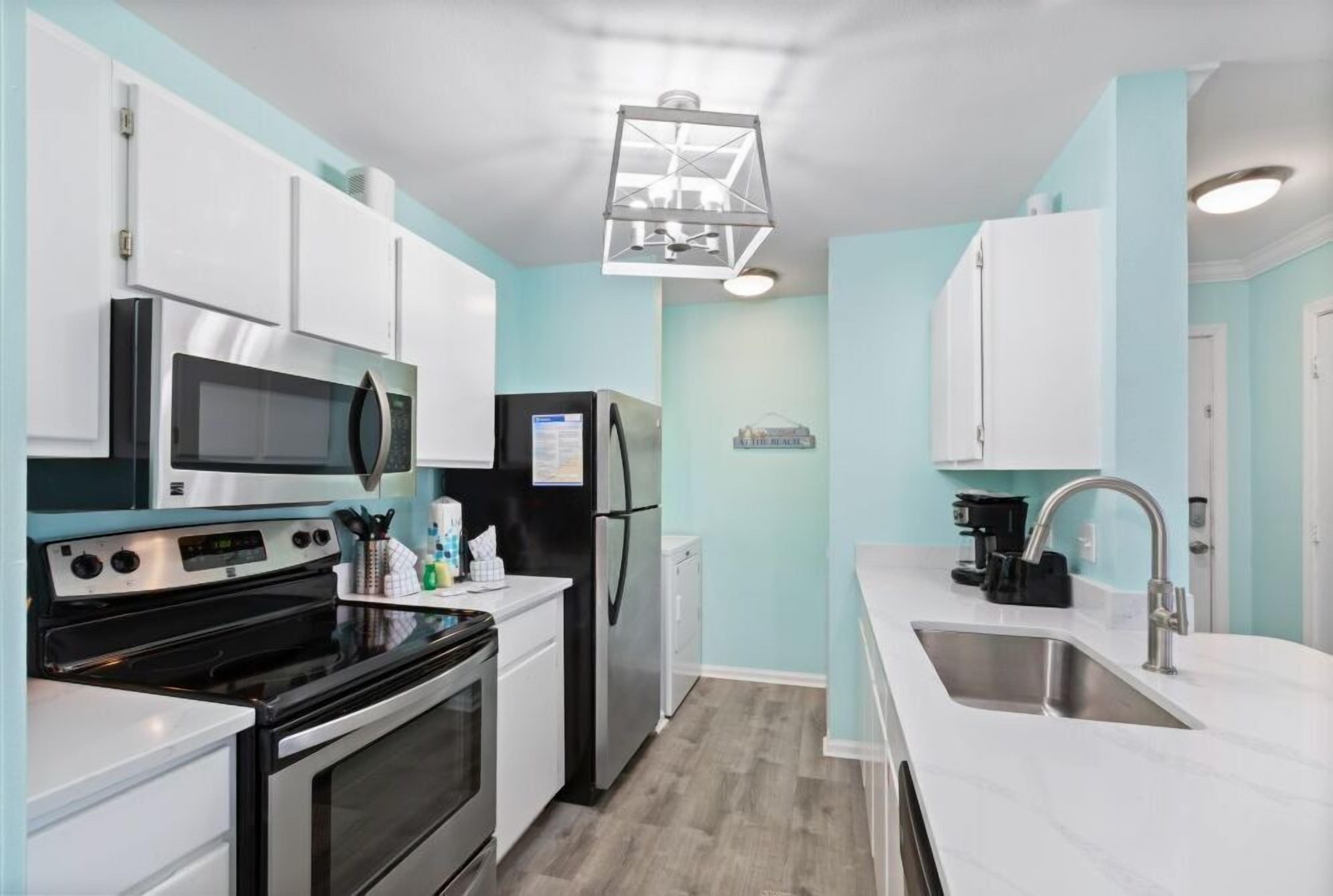 A modern kitchen with white cabinets, stainless steel appliances, and a light blue wall.