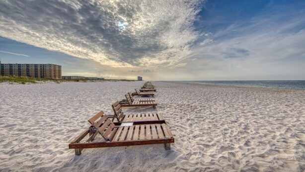Ein Strand mit in Reihen angeordneten Holzliegen, ein Gebäude in der Ferne und ein klarer Himmel.