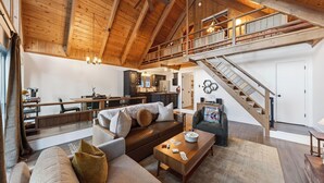A spacious loft-style living area with a high ceiling, wooden beams, a cozy seating area with a sofa and armchairs, a kitchen with dark cabinets, and a wooden staircase. - Hot Tub Firepit Loft Suite & Mins to World-class Skiing Tahoe A-frame Retreat by Avantstay (Carnelian Bay)
