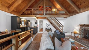 Uma ampla sala em estilo loft com escada de madeira, um espaço de estar aconchegante e uma cozinha com armários escuros.