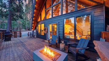 A cabin with a deck, outdoor seating, a fire pit, and large windows.
