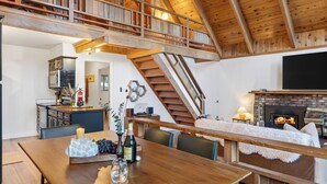 A spacious loft with a kitchen, dining area, and a fireplace. A wooden staircase connects the two levels. - Hot Tub Firepit Loft Suite & Mins to World-class Skiing Tahoe A-frame Retreat by Avantstay (Carnelian Bay)