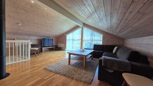 A spacious loft with wooden walls, a large window, a television, a sofa, and a small table. - Spacious mountain apartment in Sirdal, near Kjerag and the Lysefjord (Agder)