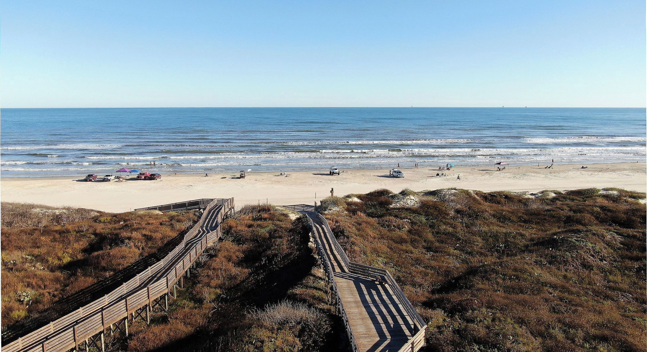 A beach with a wooden boardwalk leading to the shore, sandy beach, and the ocean.