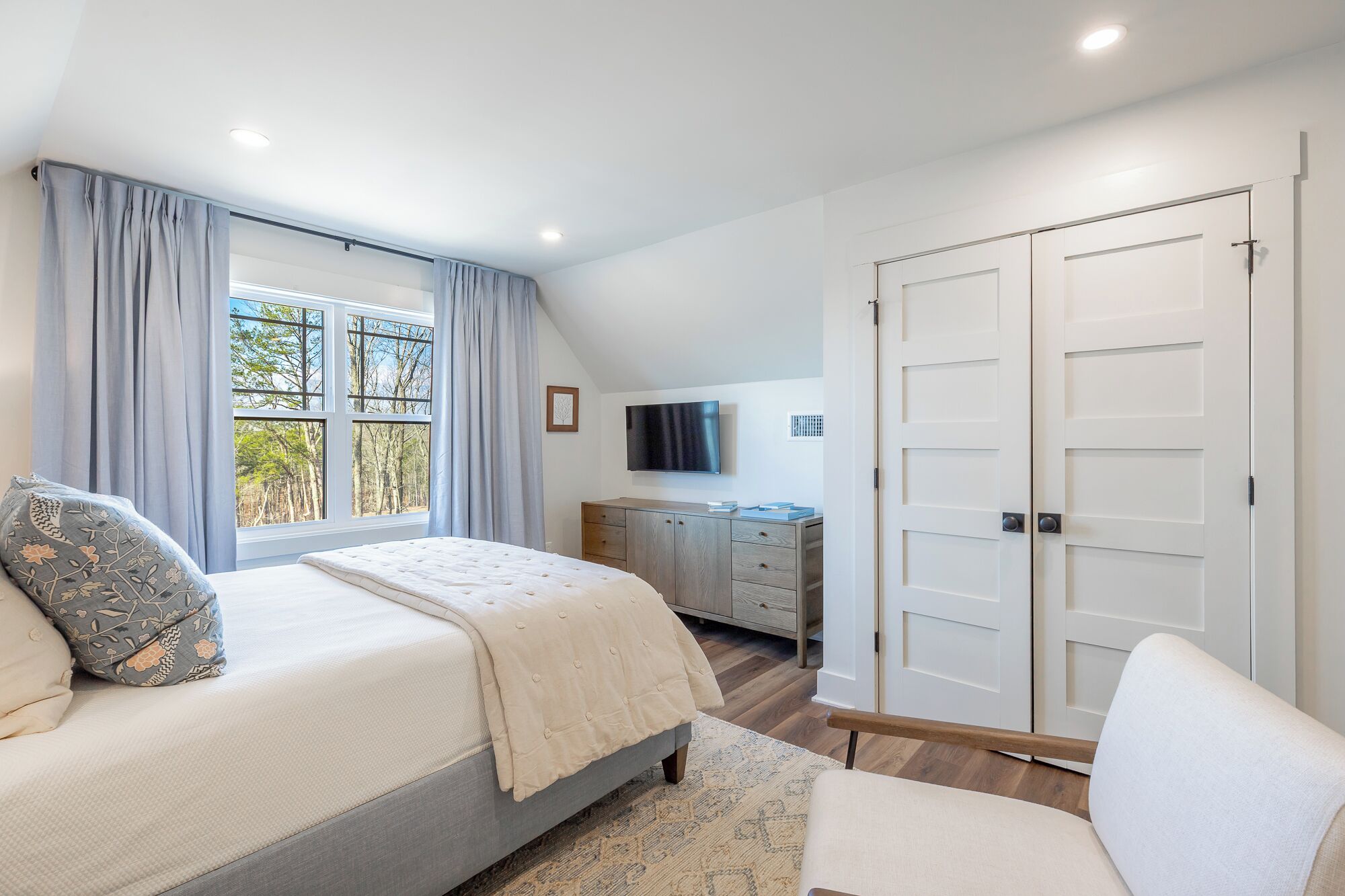 A bedroom with a large bed, a TV, a wardrobe, and a window with curtains.