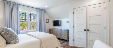 A bedroom with a large bed, a TV, a wardrobe, and a window with curtains.