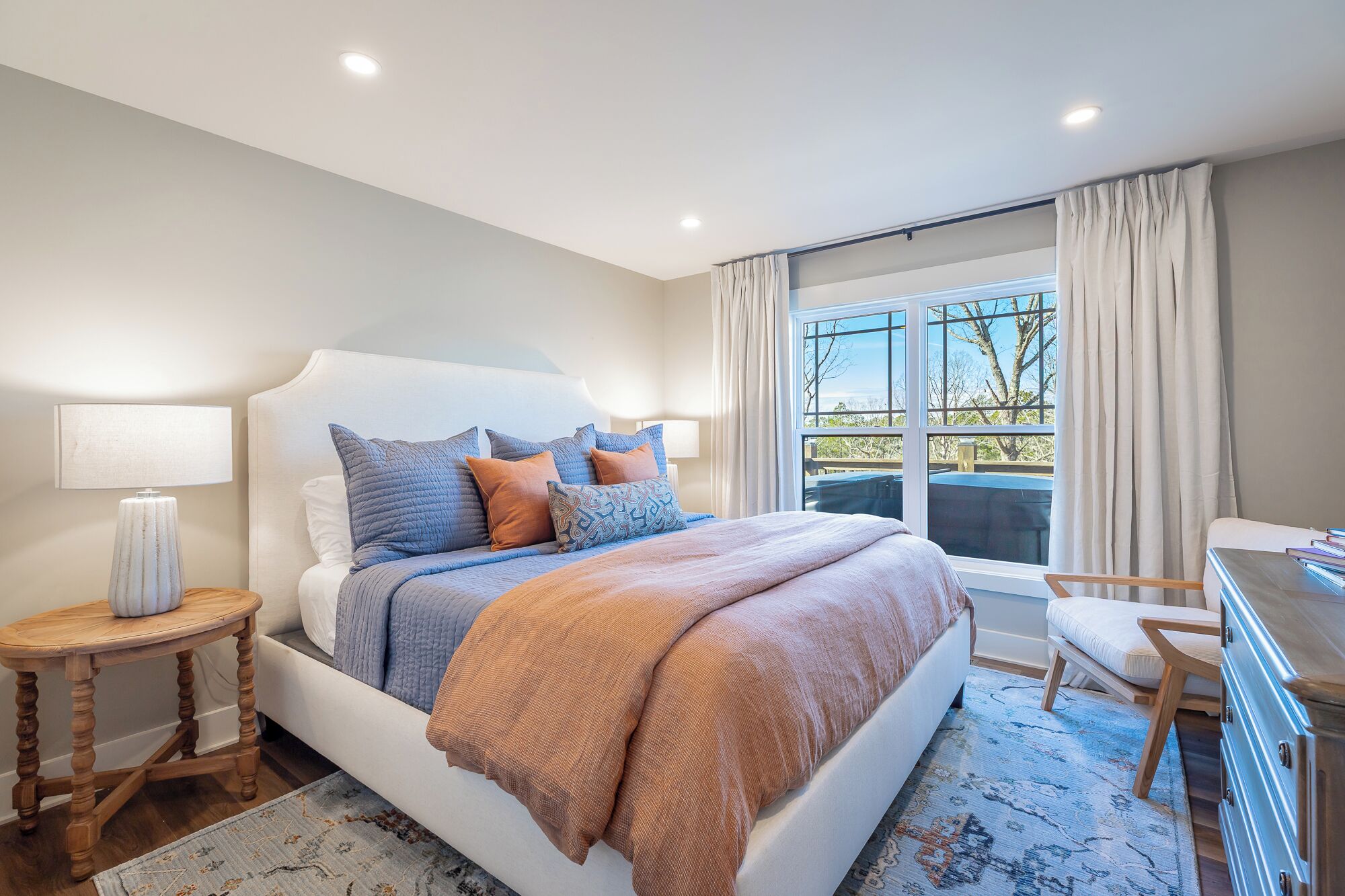 A modern bedroom with a large bed, bedside tables, a desk, and a view of the outdoors.