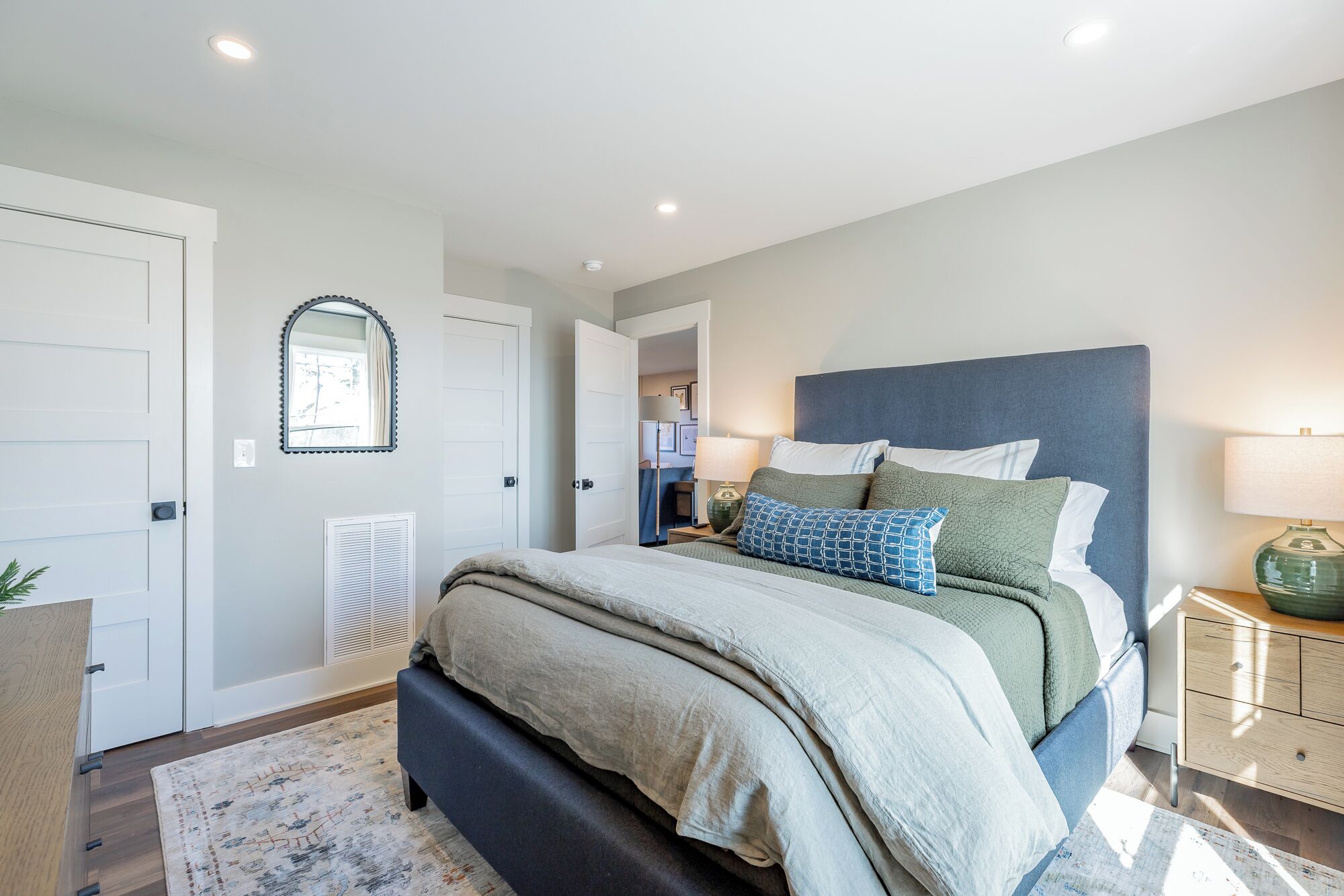 A bedroom with a bed, bedside tables, a mirror, and a door.