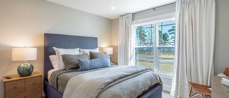 Un dormitorio con una cama grande, mesitas de noche, una lámpara y vistas al exterior.