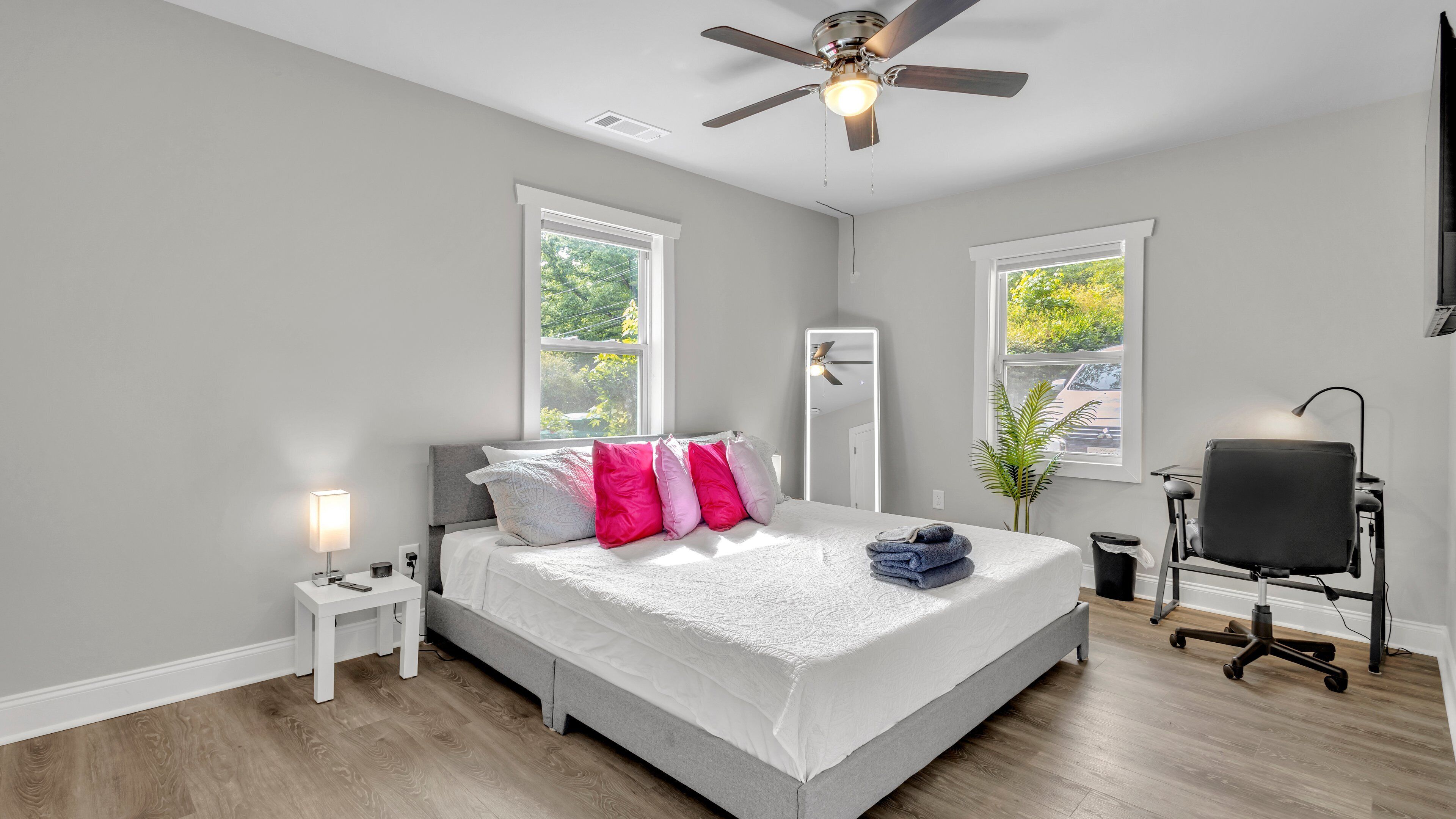Une chambre à coucher avec un lit, des tables de chevet, un ventilateur de plafond, une fenêtre et une chaise.